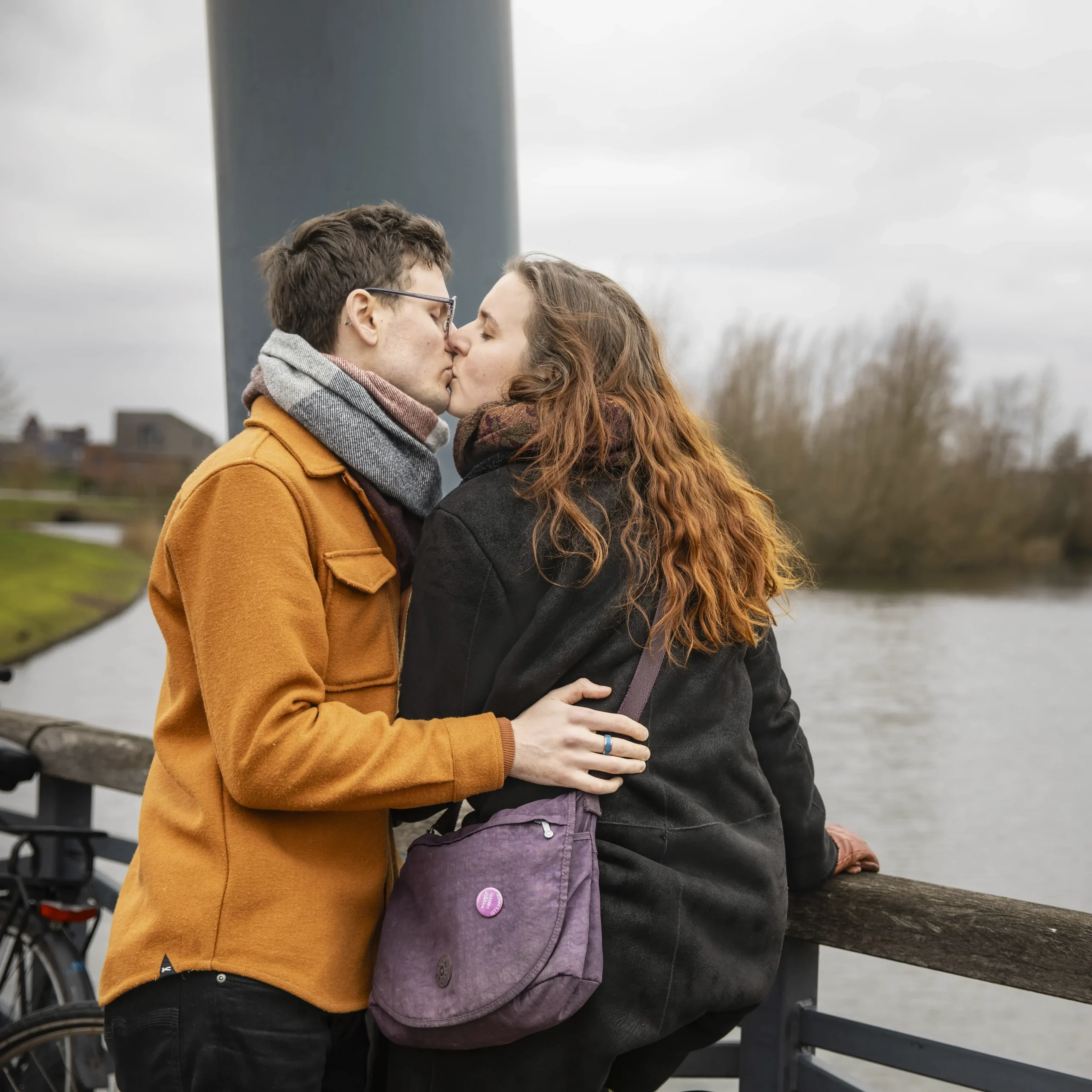 A couple, a man and a woman, kissing on a bridge with a lake visible behind them